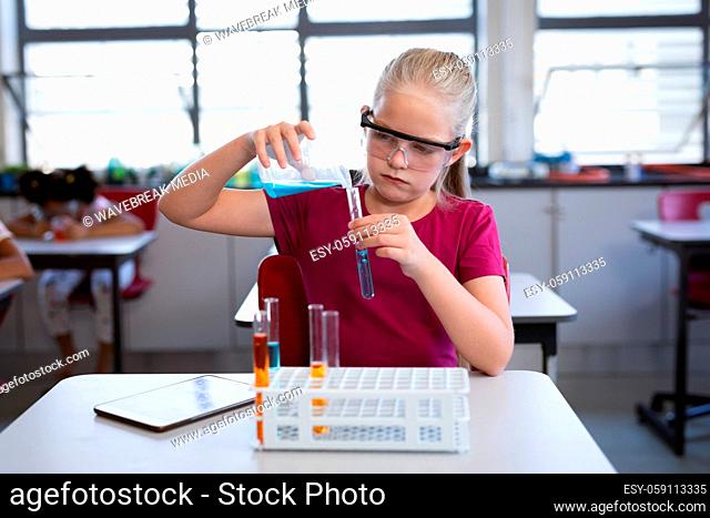 Caucasian girl pouring chemical from beaker into test tube in science class at laboratory