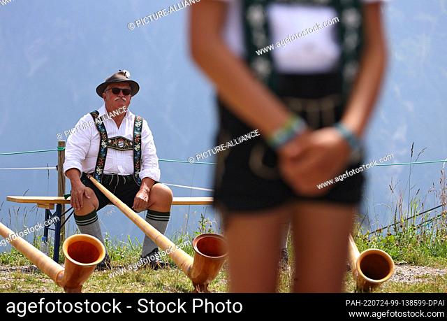 24 July 2022, Bavaria, Oberstdorf: A musician of the alphorn group EUREGIO via salina, sits behind a boy in Bavarian costume at the 30th Berglar-Kirbe on the...