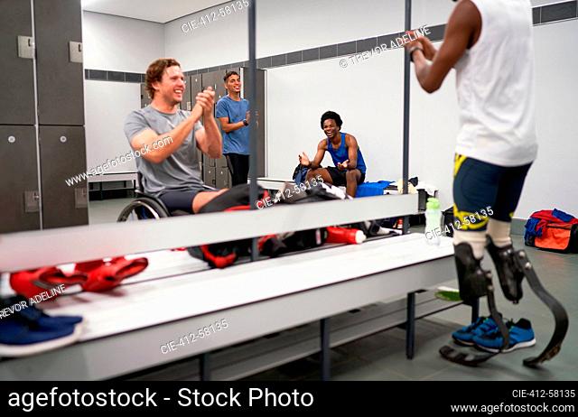 Happy amputee and wheelchair athletes clapping in locker room