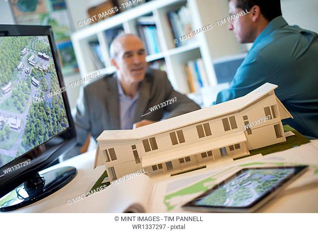 Architects working on a green construction project, using computer technology, in an office. Scale model of a building
