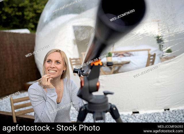 Smiling woman with telescope in front of transparent dome hotel