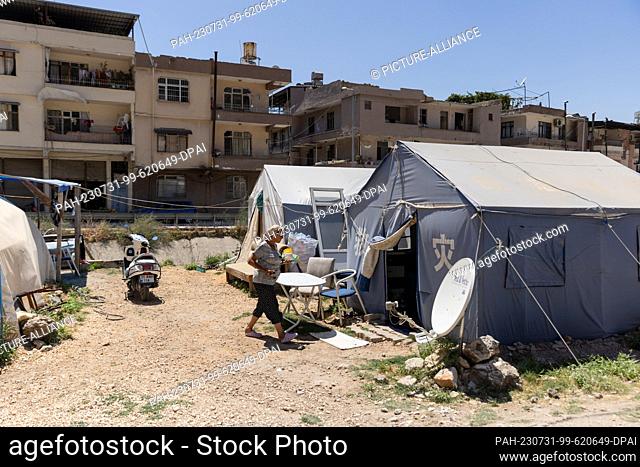 PRODUCTION - 19 July 2023, Turkey, Antakya: Ayfer Orukcu walks between her tent (r) and a flower bed in a tent city in central Antakya