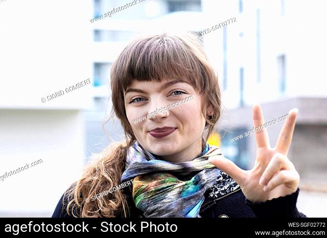 Young woman smiling while gesturing hand sign standing outdoors