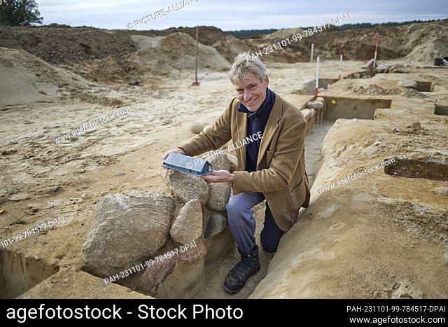 01 November 2023, Brandenburg, Seddin: Excavation leader Immo Heske, University of Göttingen, holds the model of a house in his hands during excavations of a...