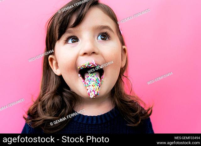 Portrait of happy little girl with sugar granules on lips and tongue in front of pink background