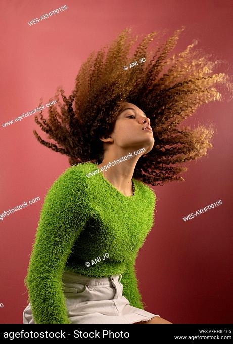 Beautiful woman tossing hair while sitting by colored background
