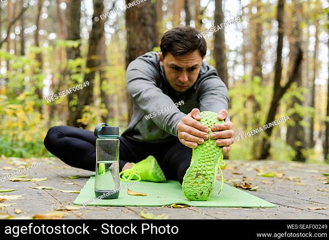 Young man stretching leg on exercise mat at park