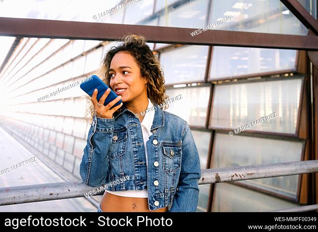 Young woman talking on speaker smart phone by railings