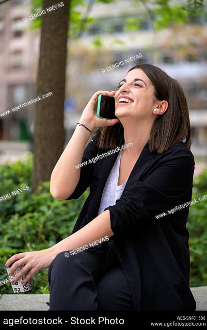 Happy young woman talking on mobile phone while sitting at park