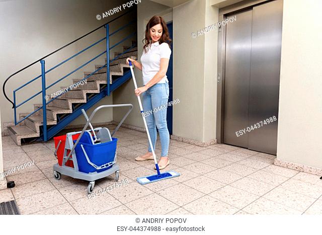 Smiling Young Female Janitor Cleaning Floor In Corridor With Mop