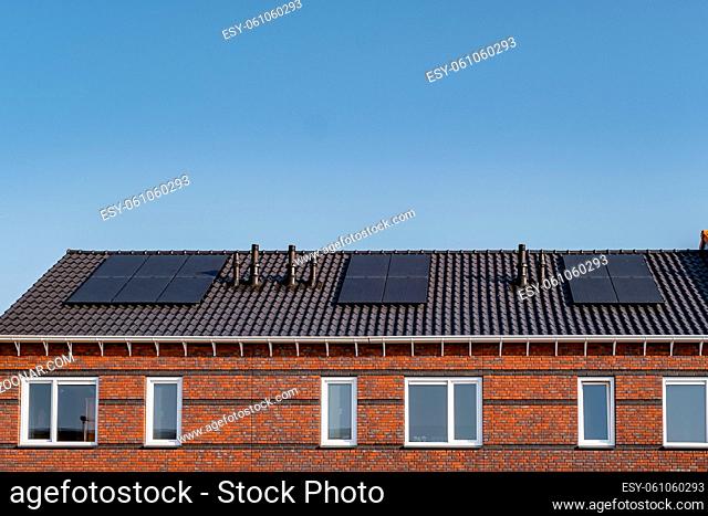 Newly build houses with solar panels attached on the roof against a sunny sky Close up of new building with black solar panels
