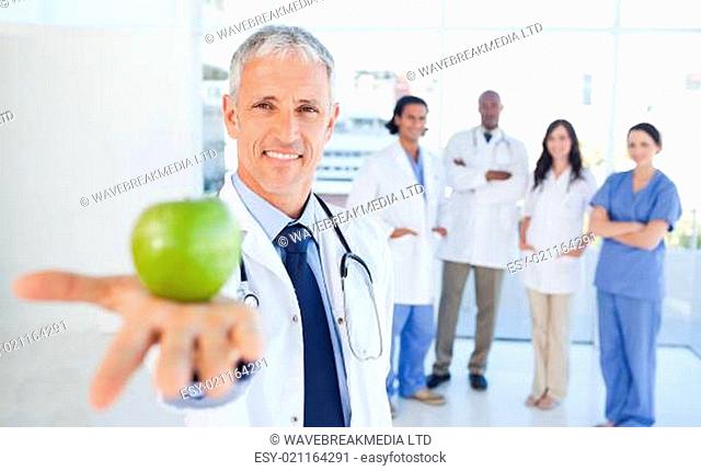 Medical interns in the background looking at their doctor who is holding an appl