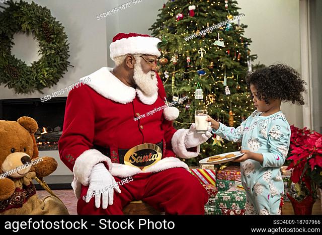 Shy seven year old handing milk and cookies to Santa Claus