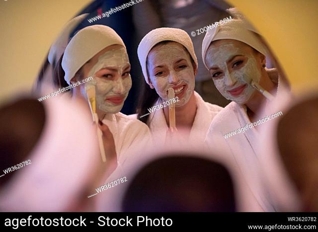 a group of young beautiful women looking in the mirror while putting face masks in the bathroom