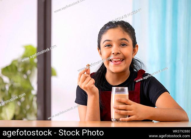 Portrait of cheerful little girl having breakfast with cereal and chocolate milkshake at home