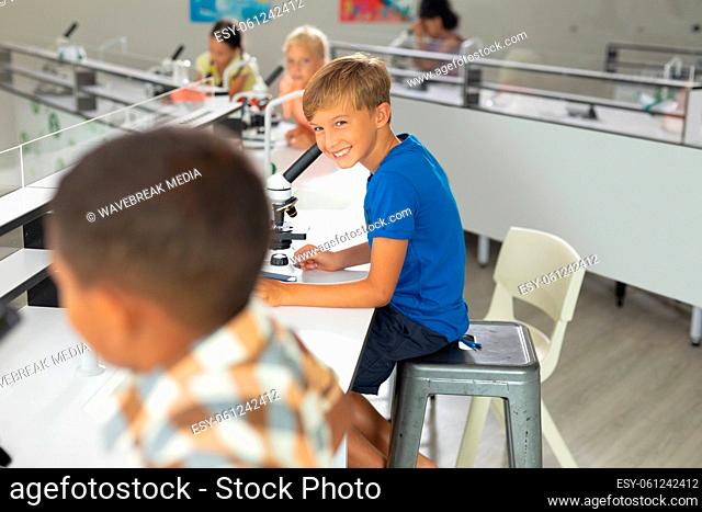 Smiling caucasian elementary boy looking at biracial male classmate in laboratory