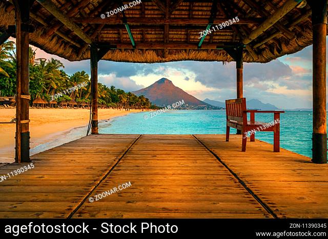Wonderful view across the pier, on the left the tropical beach and in the background a beautiful mountain illuminated by red during sunset, Mauritius