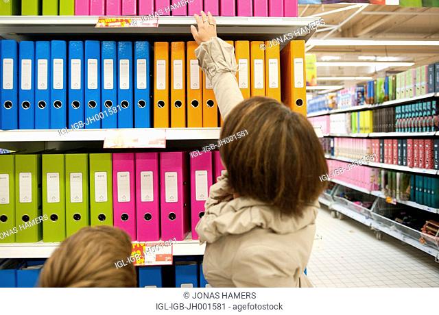 A mother and her two children shopping and buying elementary school supplies in a supermarket