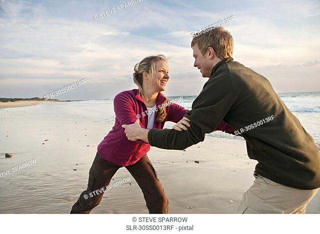 Young man and woman wrestling at beach