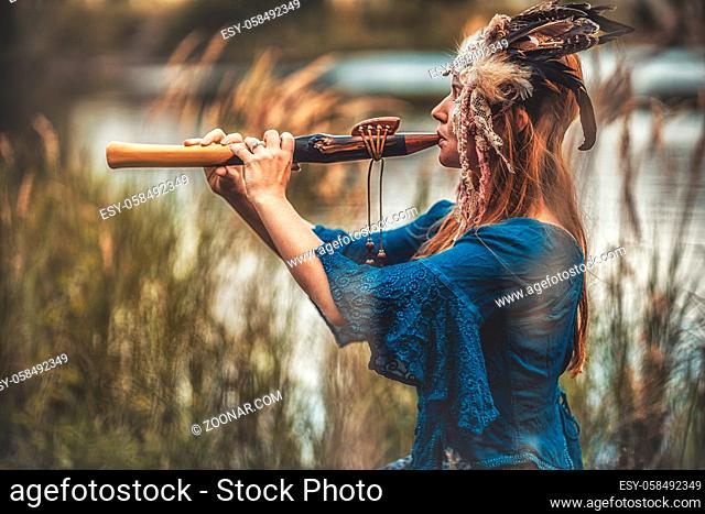beautiful shamanic girl playing on shaman flute in the nature
