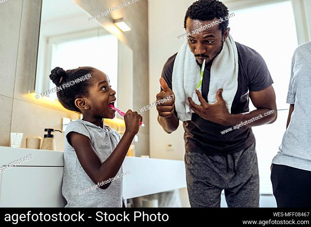 Father doing thumbs up to daughter brushing teeth in bathroom