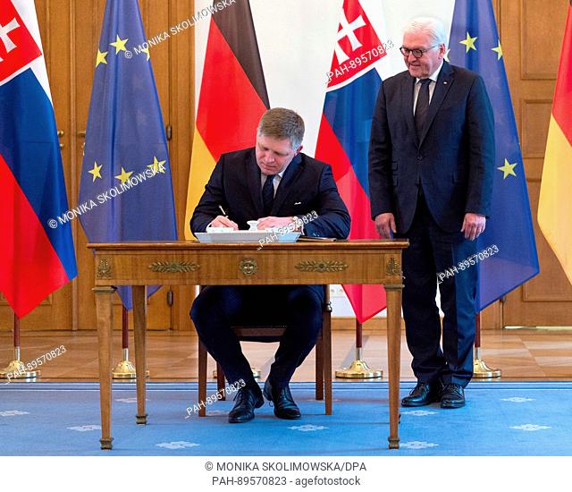 Slovakian Prime Minister Robert Fico (C) signs the guestbook, with German President Frank-Walter Steinmeier (R) looking on