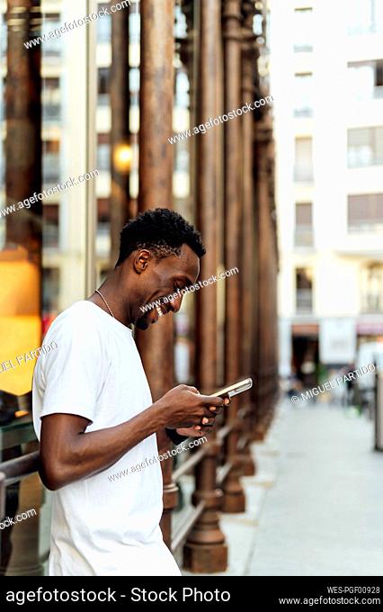 Smiling young man using mobile phone in city