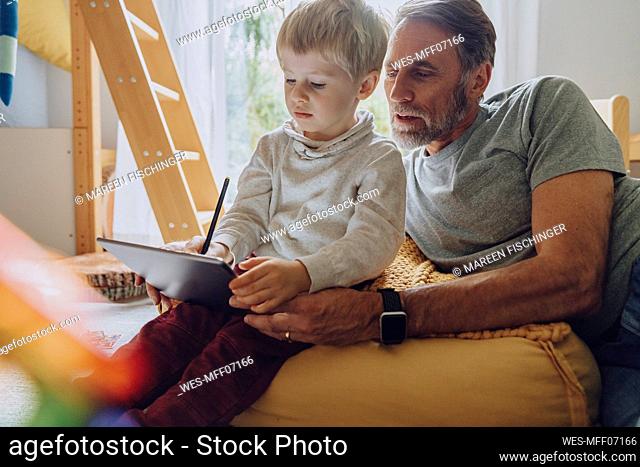 Father looking son using digital tablet computer in bedroom