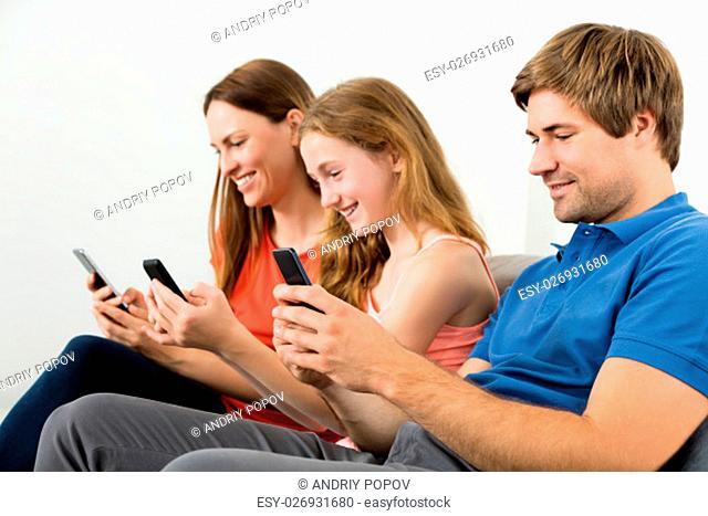 Smiling Family Sitting On Sofa Using Mobile Phone