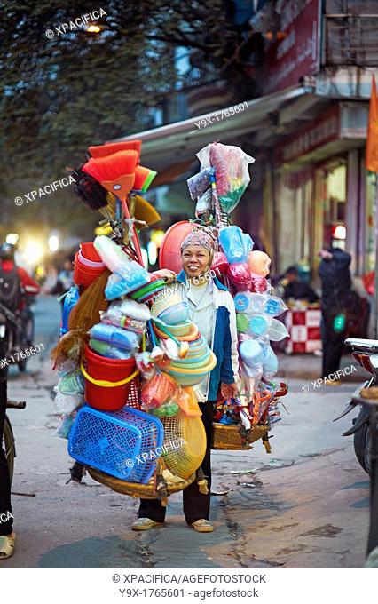 A woman selling plastic goods on the street balancing them on baskets on her shoulder