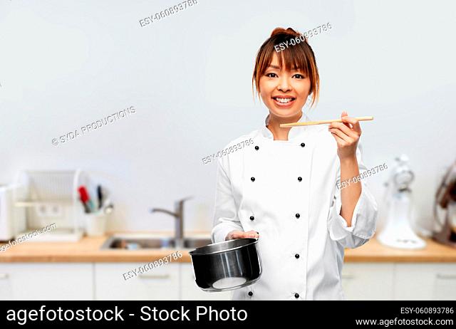 female chef with saucepan tasting food on kitchen