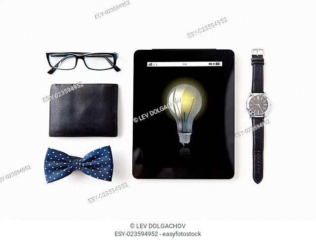 technology and objects concept - tablet pc computer with light bulb icon, wallet, eyeglasses, bowtie and wristwatch on table