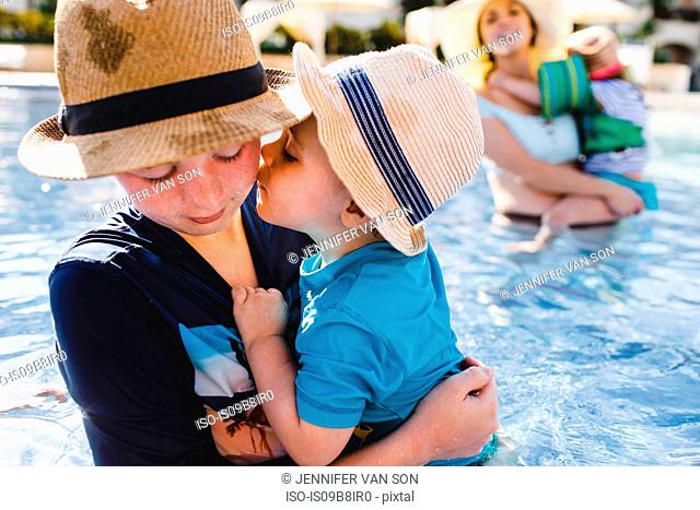 Family in outdoor swimming pool, young boy holding younger brother