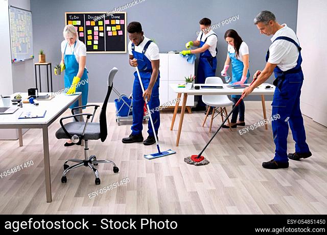 Group Of Janitors In Uniform Cleaning The Office With Cleaning Equipment