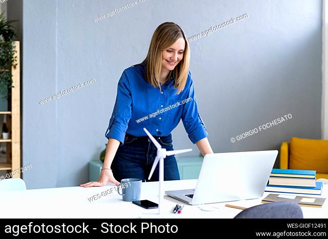 Businesswoman smiling while looking at laptop in office