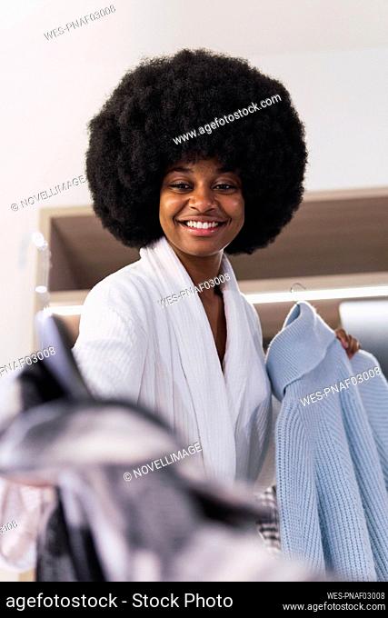 Smiling Afro woman holding clothes at home