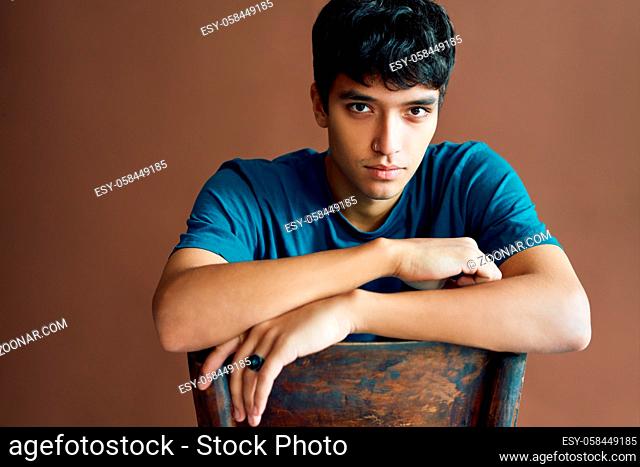 Stylish handsome young man posing on studio sitting on a chair looking to camera. man beauty concept
