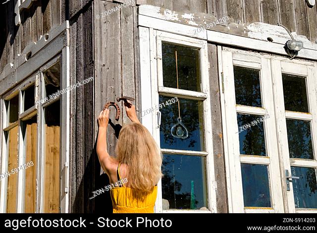 Woman in yellow dress hang horse shoe symbol of luck on country house wall