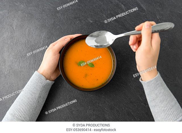 hands with bowl of pumpkin cream soup on table