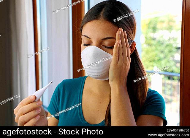 COVID-19 Pandemic Coronavirus Mask Fever Woman Checking Temperature with Thermometer at Home Symptom of SARS-CoV-2. Girl with mask on face check fever one of...