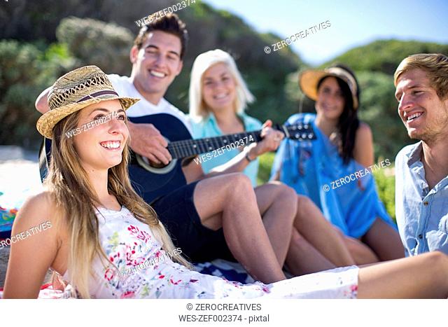 Friends socializing on the beach and playing acoustic guitar
