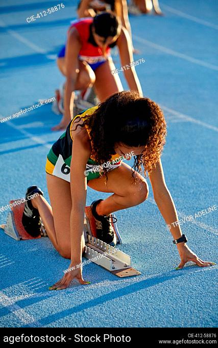 Female track and field athletes preparing at starting blocks on track