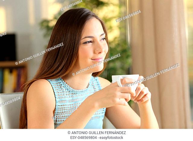 Happy woman relaxing looking at side holding coffee cup at home