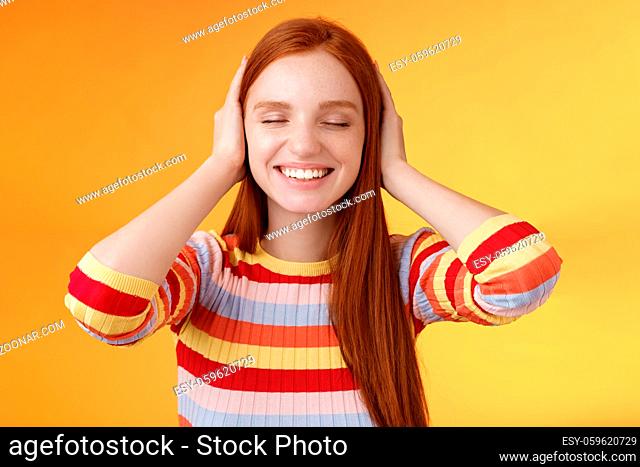 Dreamy charismatic relaxed tender redhead caucasian girl 20s close eyes cover ears imaging far away, smiling broadly enjoy silence peace comfort without sounds...