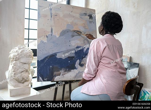 Artistry. A dark-skinned woman sitting near the easel and painting