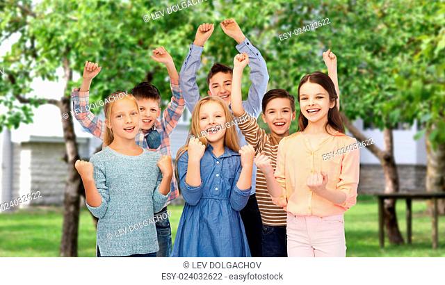 childhood, fashion, gesture and people concept - happy children friends raising fists and celebrating victory over private house backyard background