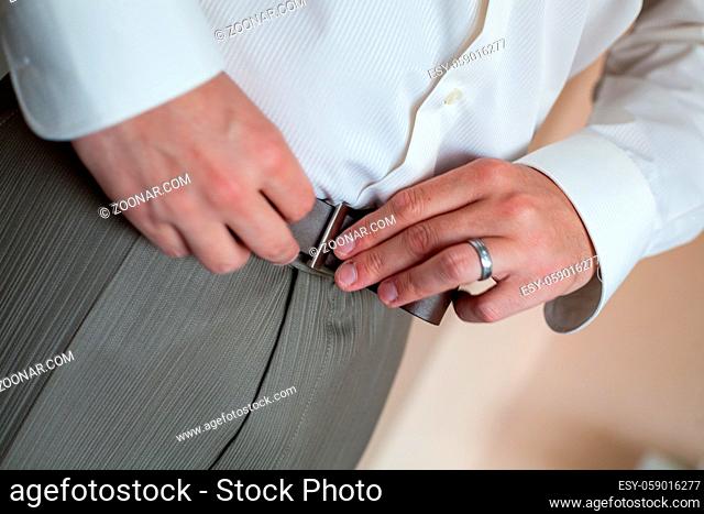 A man in pants and shirt buttoned a black leather trouser belt. Groom Dress up a belt with buckle. Businessman wear leather stylish belt