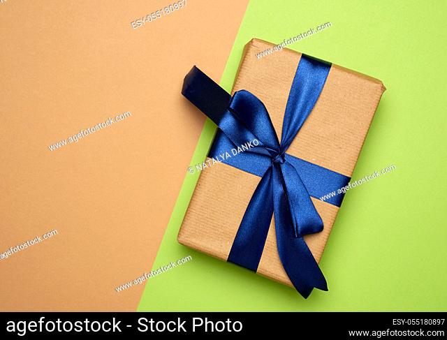 rectangular box wrapped in brown paper and tied with a silk ribbon with a bow, gift on a green background, top view, copy space