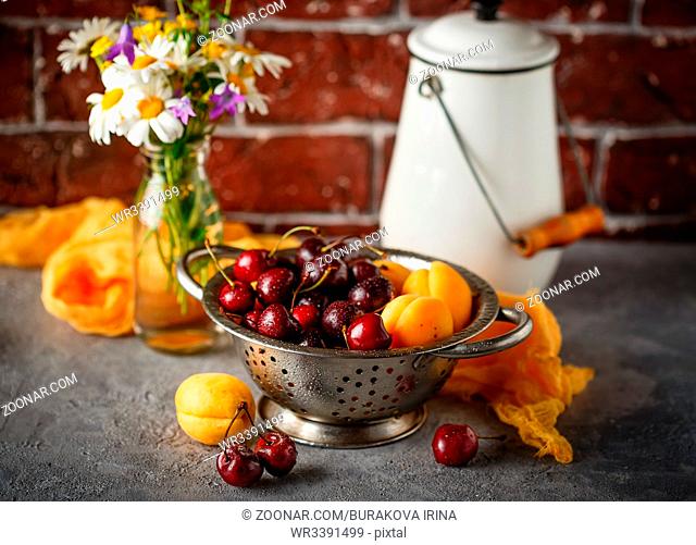 Fresh sweet cherries and apricots in metal colander