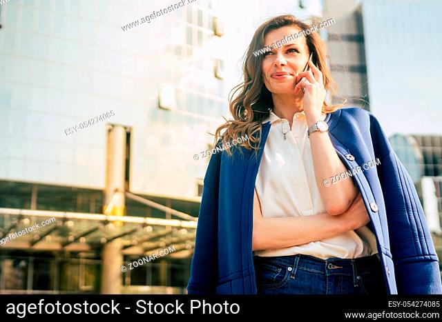 Caucasian business woman speaking by phone. Waist up portrait of a successful European business woman woman, talking on the phone, standing on glass background